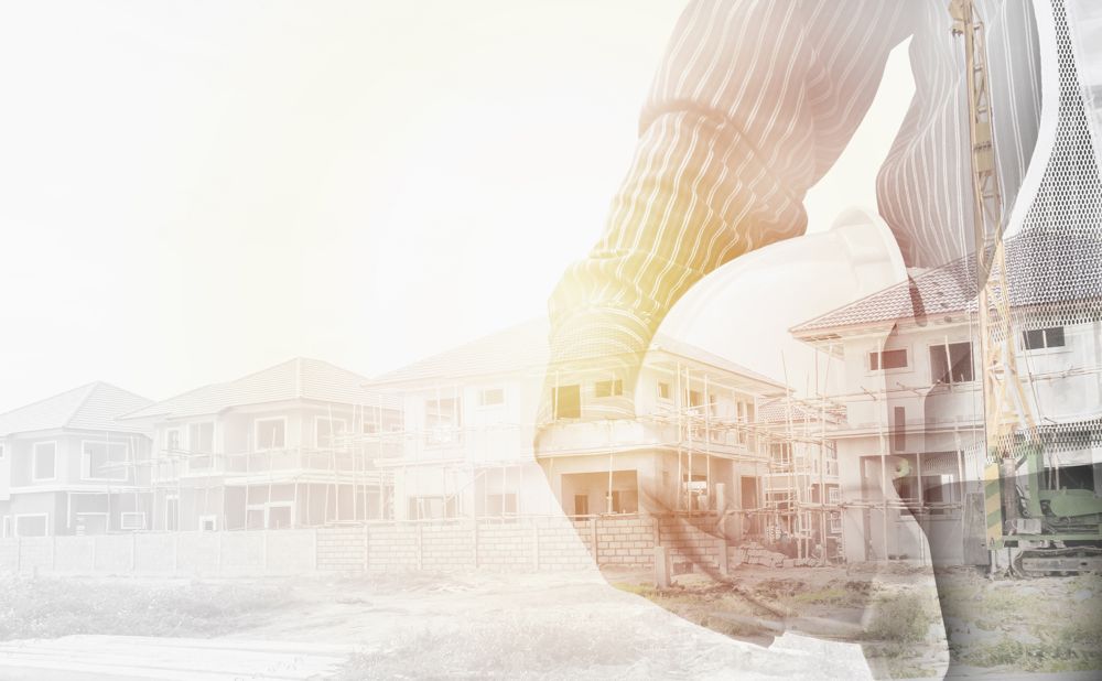 A person in a striped shirt holding a white hard hat is superimposed over a background of residential houses under construction, with scaffolding and building equipment visible.