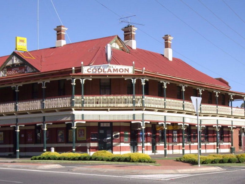 A two-story historic building with a red roof and cream trims, featuring wraparound balconies and a sign that reads 